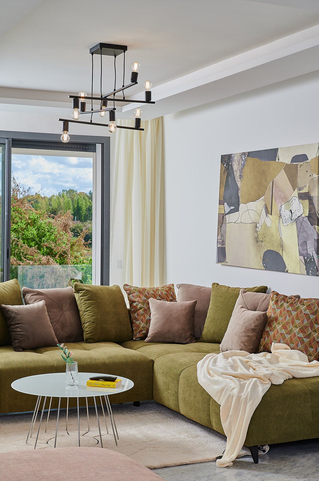 A modern living room with a green sectional sofa, a white coffee table, and a large abstract painting on the wall.