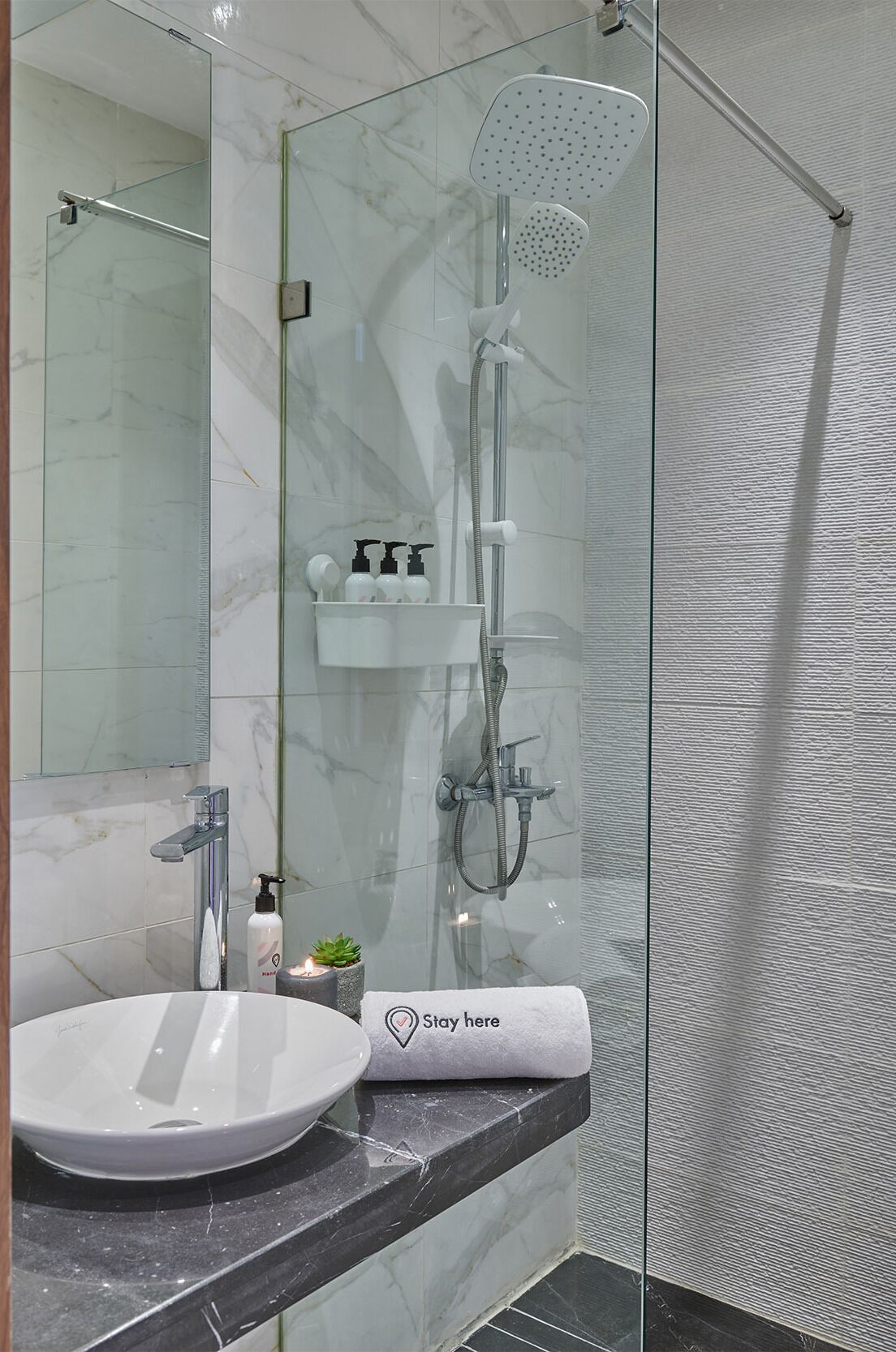 A modern bathroom with a glass-enclosed shower, a white sink, and a towel with "Stay here" written on it.