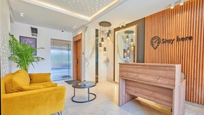 A modern reception area with a wooden reception desk, a yellow sofa, a small table, and an elevator.