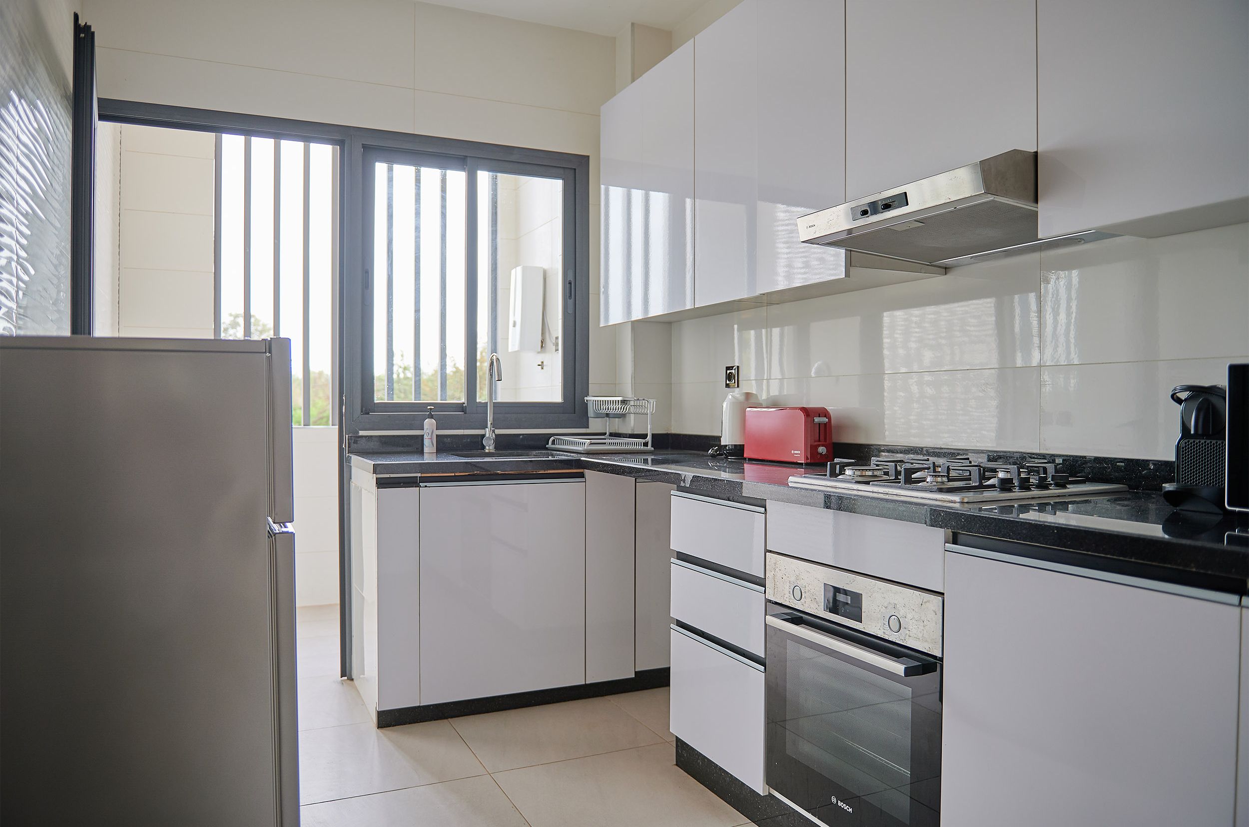 A modern kitchen with white cabinets, a black countertop, a red toaster, and a stainless steel range hood.