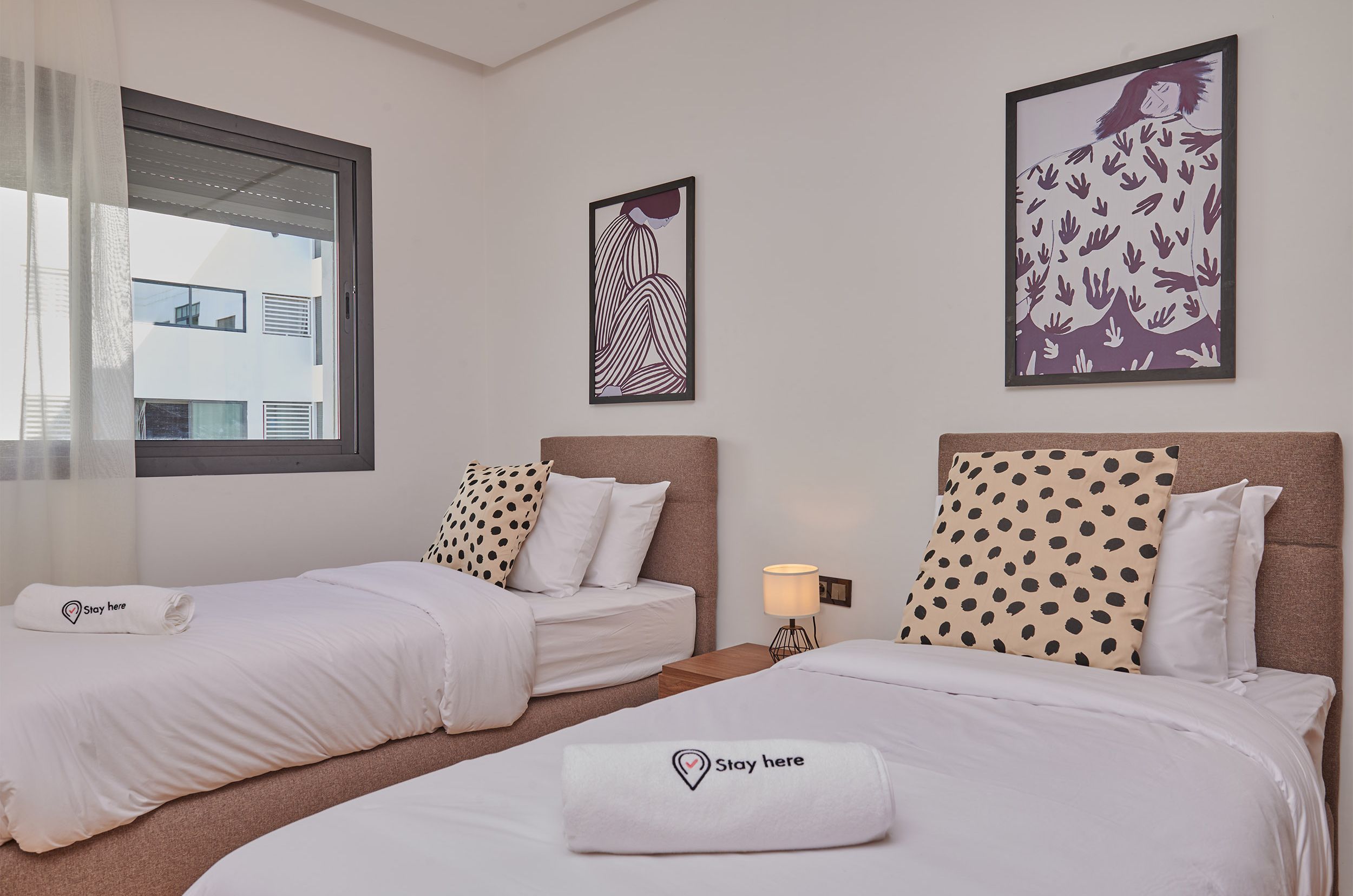 Una habitación de hotel con dos camas, una ventana con cortinas y obras de arte en las paredes.
