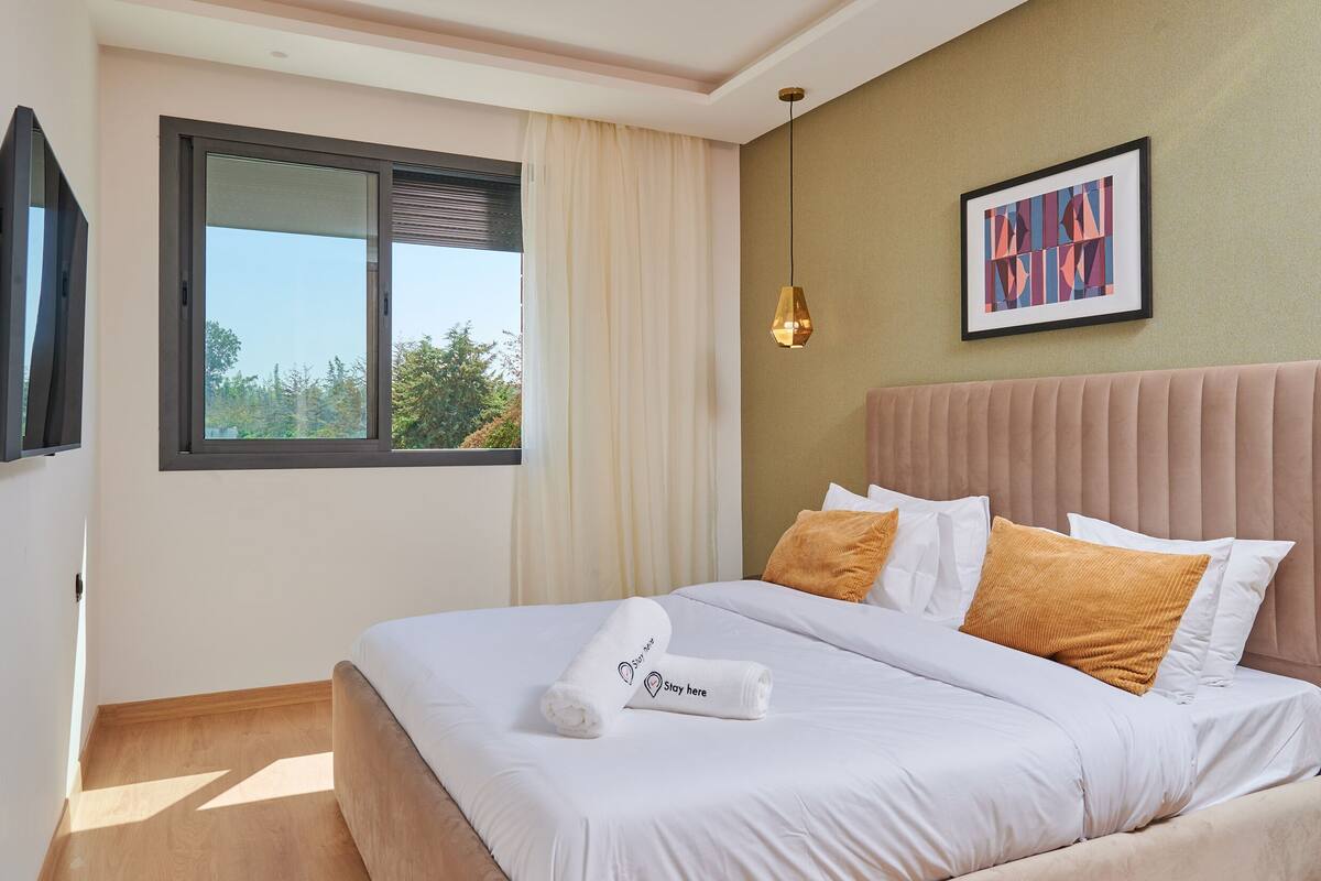 A neatly made bed with white linens and two towels, a beige headboard, and a framed picture on the wall.