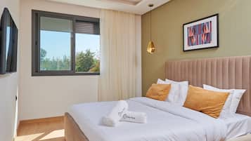 Una camera d'albergo con un letto, una finestra con tende, un quadro appeso al muro e una lampada a sospensione.