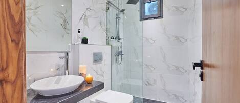 A modern bathroom with a marble sink, a toilet, and a glass-enclosed shower.