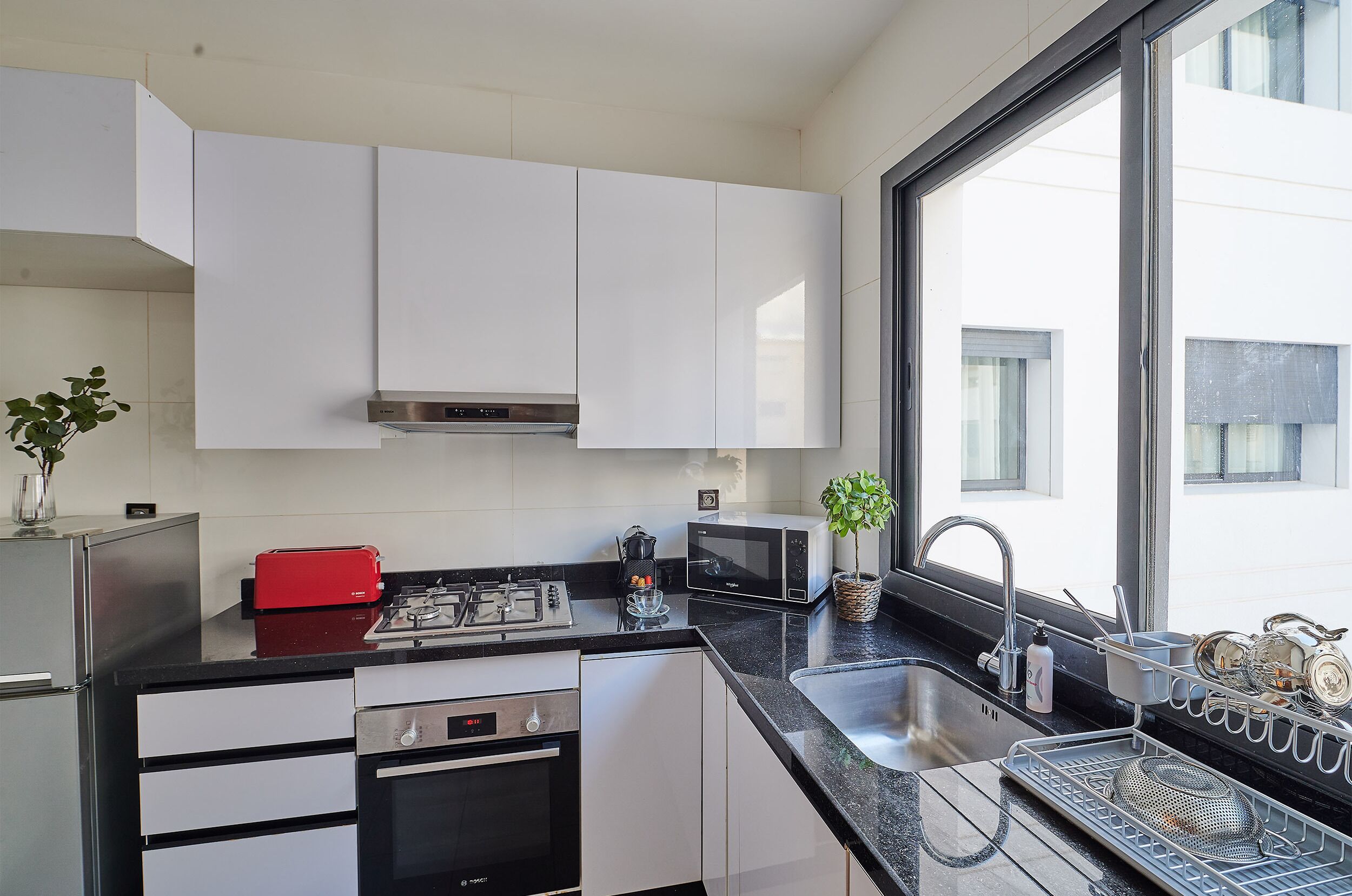 A modern kitchen with white cabinets, a gas stove, a microwave, and a sink.