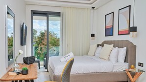A modern hotel room with a bed, a desk, a chair, and a balcony with a view of trees.