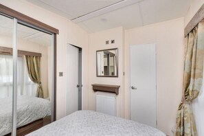 A bedroom with a bed, a mirror, a radiator, and a door. - Spacious Stunning Lakeside 3 bed Holiday Home (Northampton)