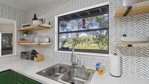 A kitchen with a double sink, wooden shelves, and a window with a view of greenery. - Beautiful, relaxing & Peaceful (Huntsville)