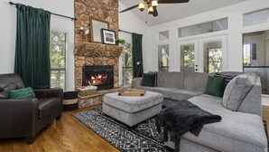 A living room with a stone fireplace, a ceiling fan, and a large window with blinds. - Beautiful, relaxing & Peaceful (Huntsville)