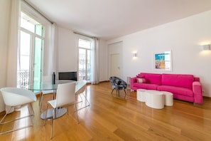Ein modernes Wohnzimmer mit einem Glastisch, weißen Stühlen, einem schwarz-weißen Armlehnstuhl, einem rosa Sofa und einem Poster an der Wand.