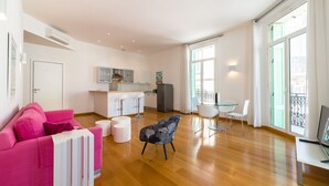 Een moderne woonkamer met een roze bank, een glazen eettafel en een keuken op de achtergrond.