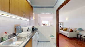 A modern kitchen with a sink, toaster, and microwave. There is a dining area with a white sofa and a lamp.