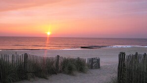 Une plage avec une clôture en bois au premier plan et le soleil se couchant sur l’océan.