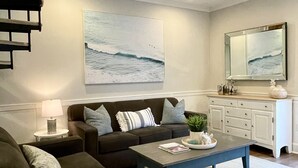 Un salon avec un canapé, une table basse et un tableau représentant l’océan.