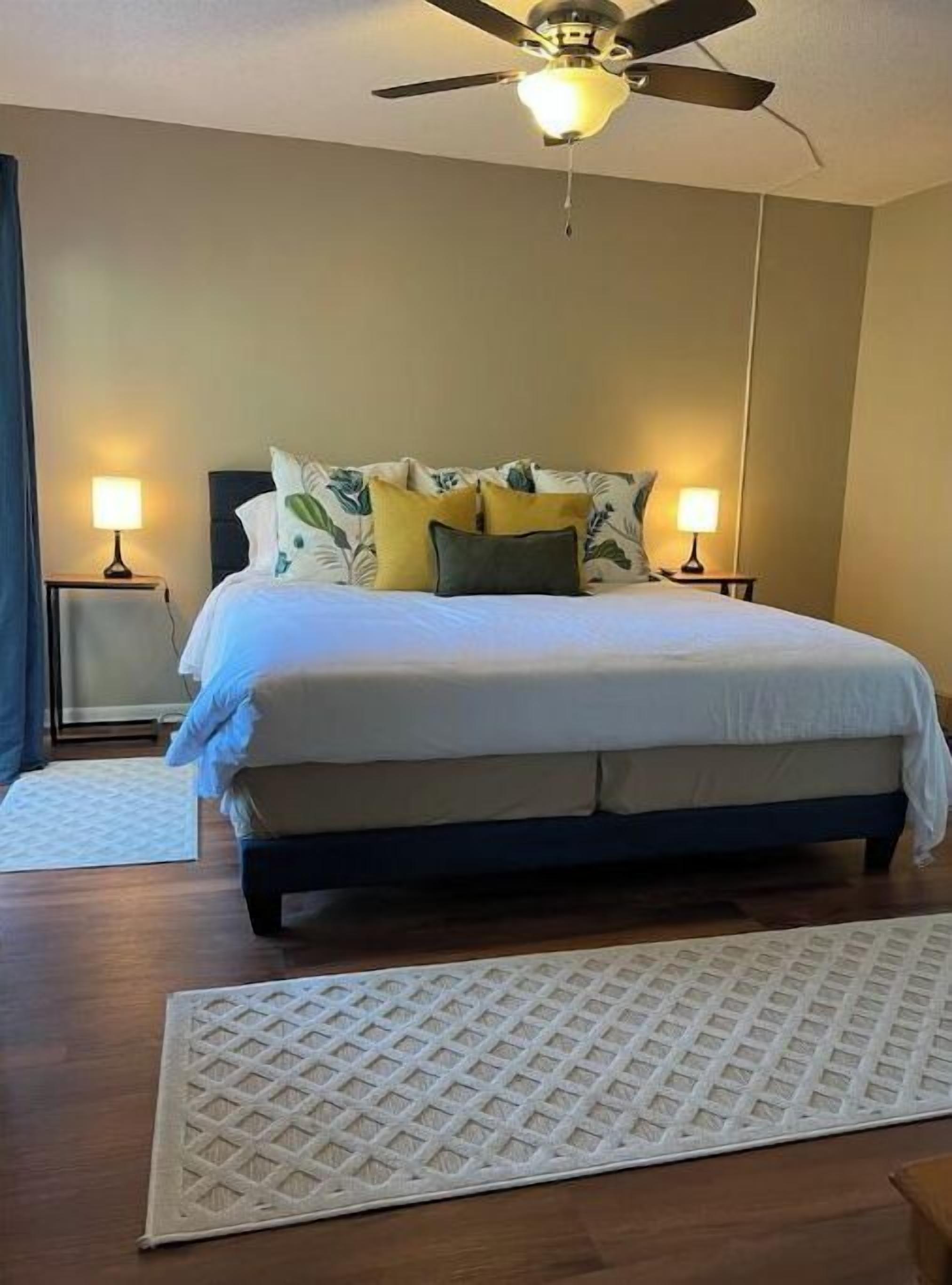 A bedroom with a bed, two bedside lamps, a ceiling fan, and a rug.