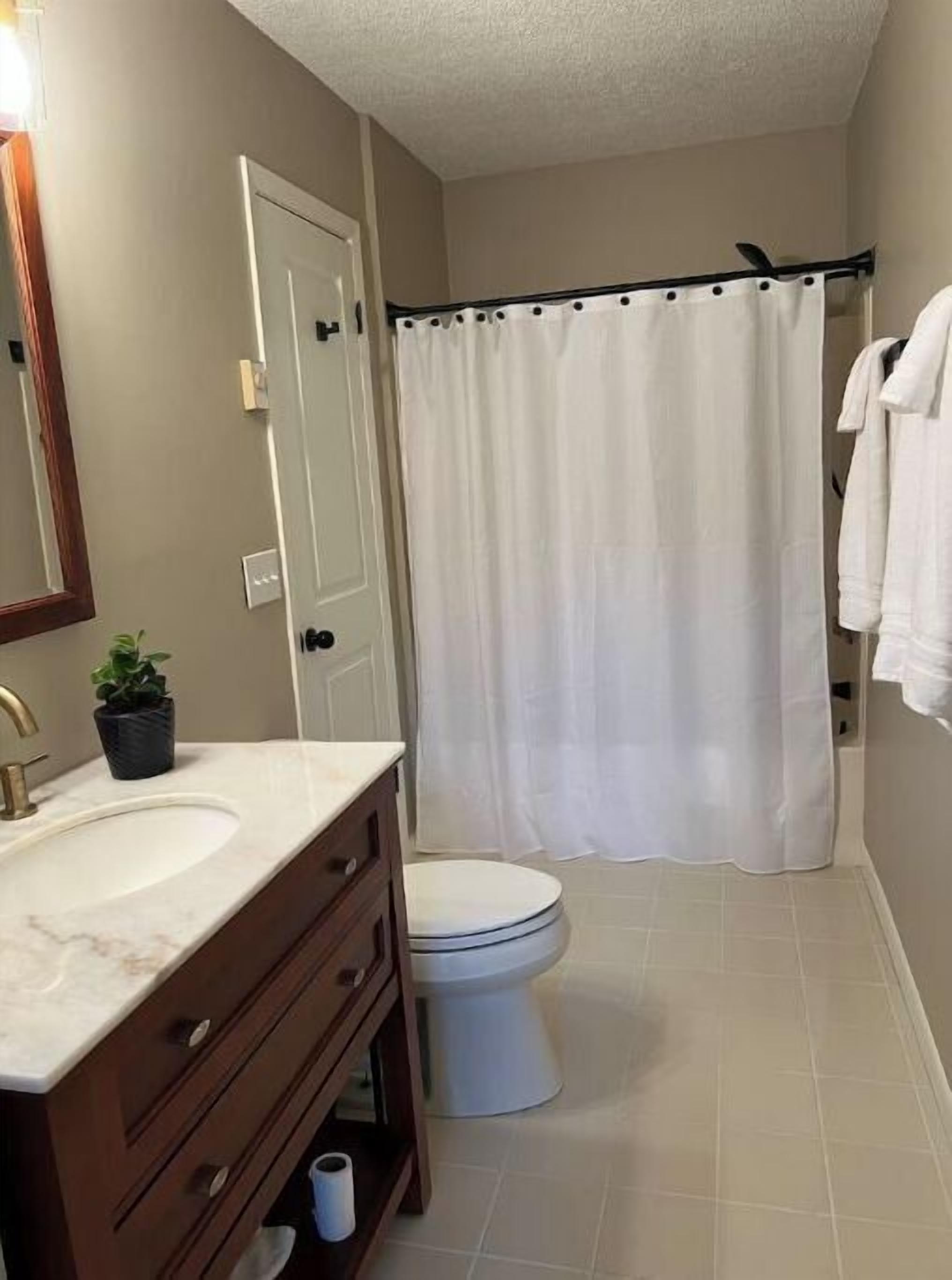 Een badkamer met een witte wastafel, een donker houten wastafelmeubel, een wit toilet en een witte douchegordijn.