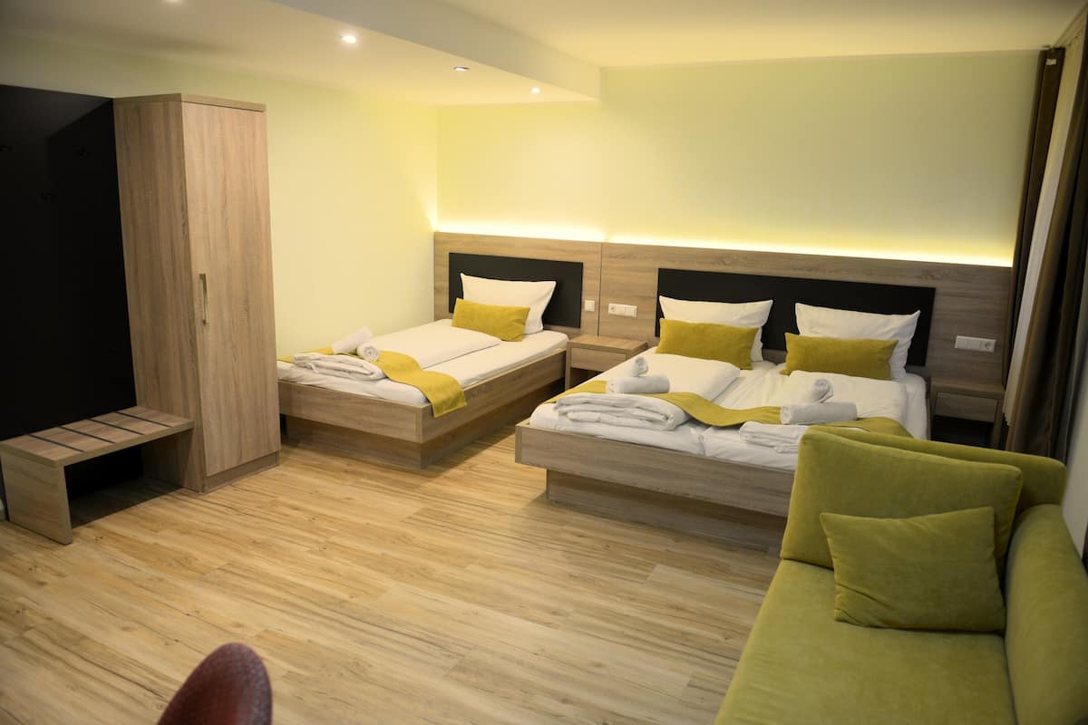 A hotel room with two beds, a sofa, a wardrobe, and a TV.