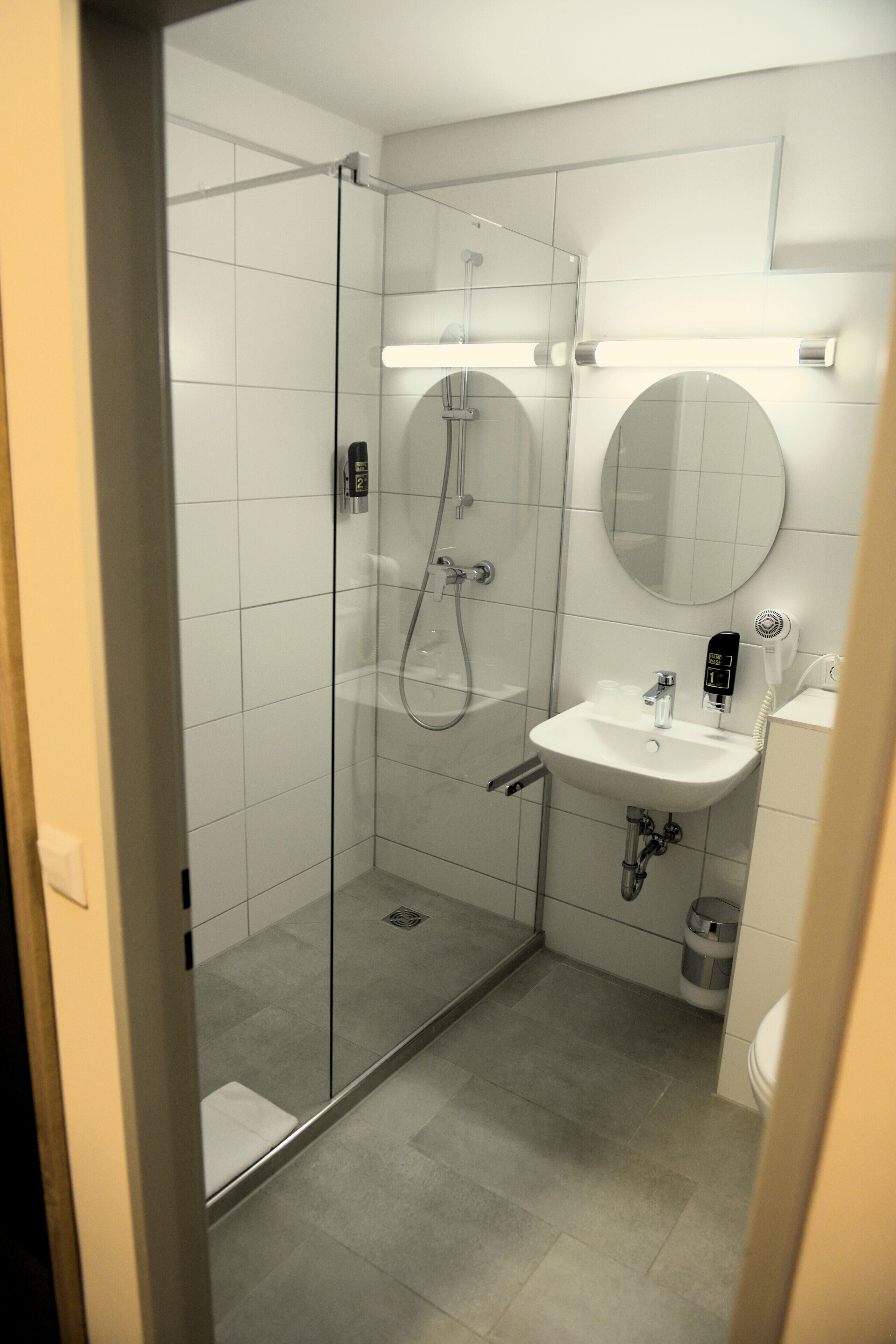 A modern bathroom with a glass-enclosed shower, a white sink, and a round mirror.