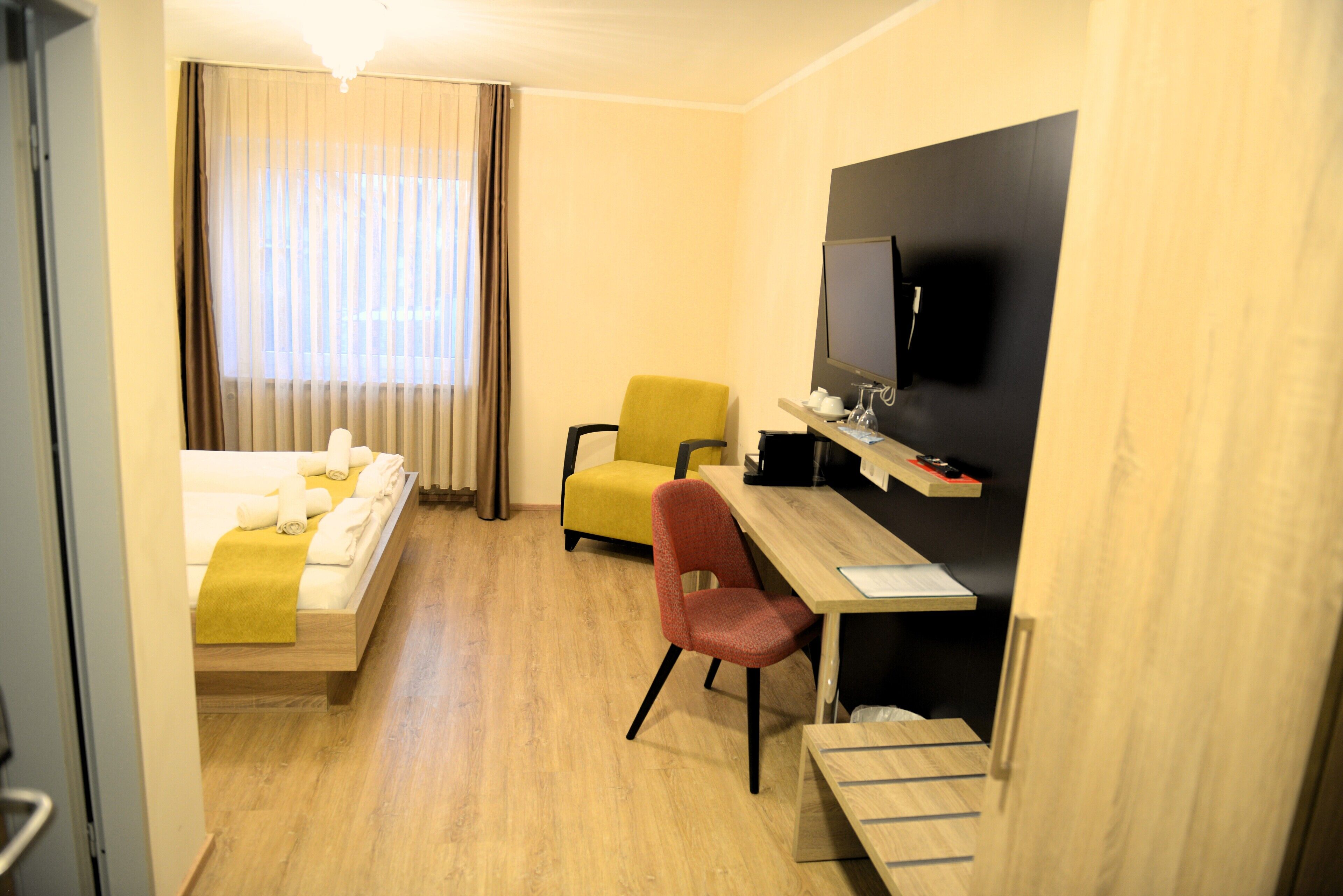 Ein Hotelzimmer mit einem Bett, einem Schreibtisch mit Stuhl, einem Fernseher und einem Fenster mit Vorhängen.