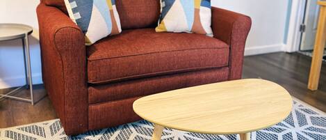 A red sofa with patterned cushions, a small wooden side table, and a geometric patterned rug.