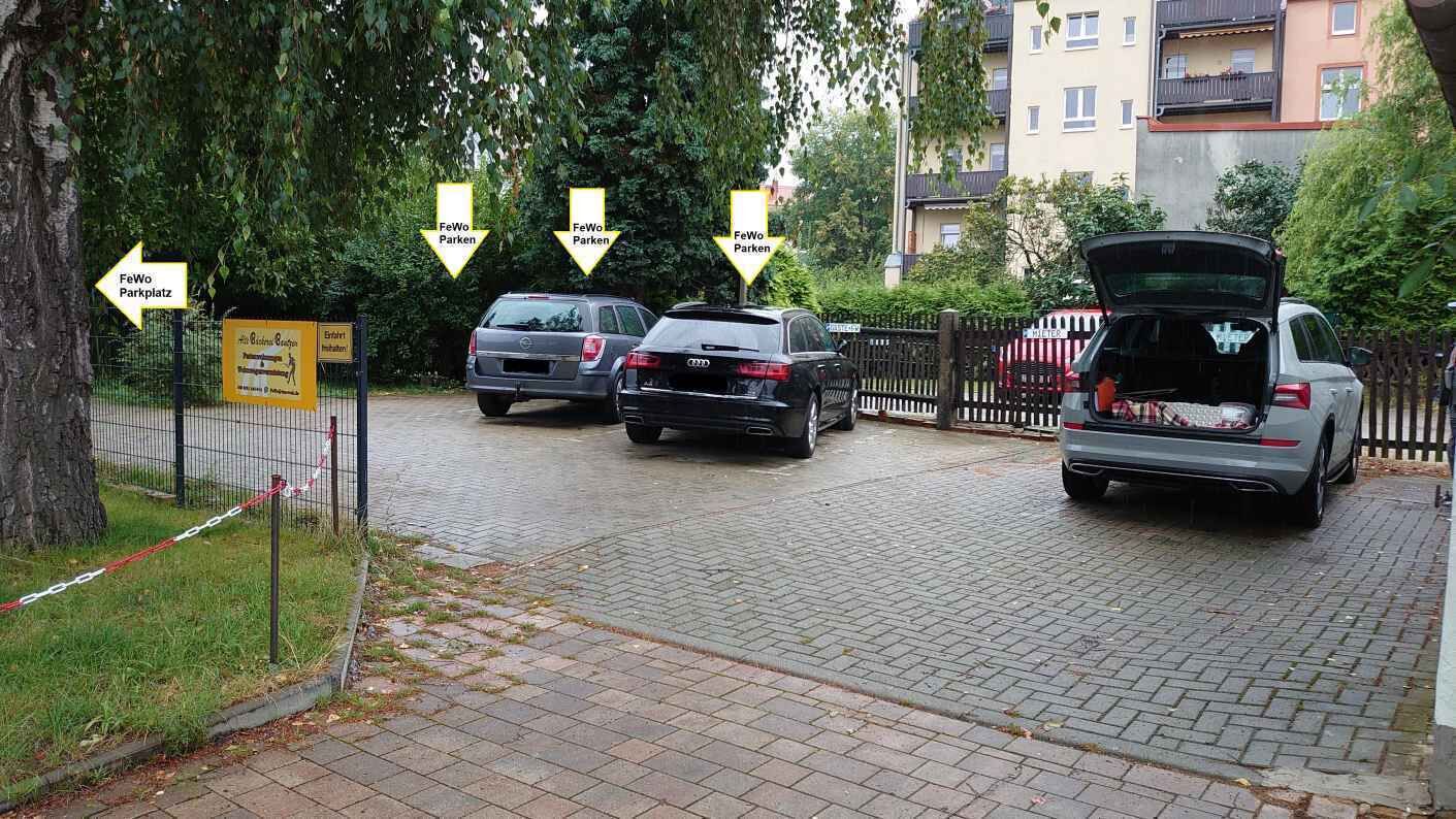 A parking area with cars and a sign indicating 'FeWo Parkplatz'.