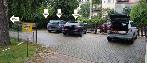 A parking area with cars and a sign indicating 'FeWo Parkplatz'.