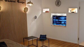 Une chambre moderne avec un mur lambrissé en bois, un petit bureau avec un ordinateur portable, un téléviseur fixé au mur et une porte dotée d’un miroir.