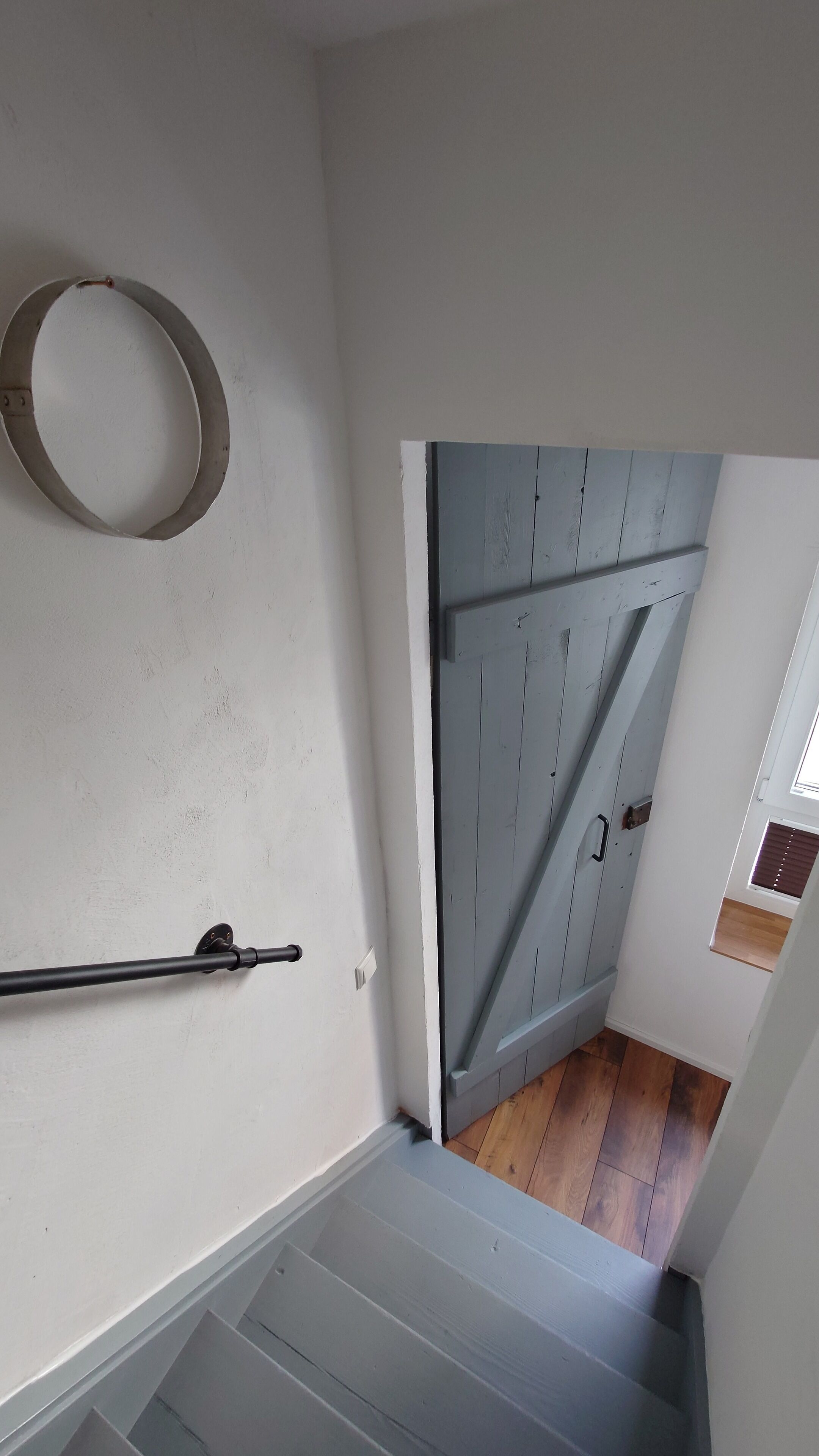 A staircase with a metal handrail, a wooden door, and a circular object on the wall.