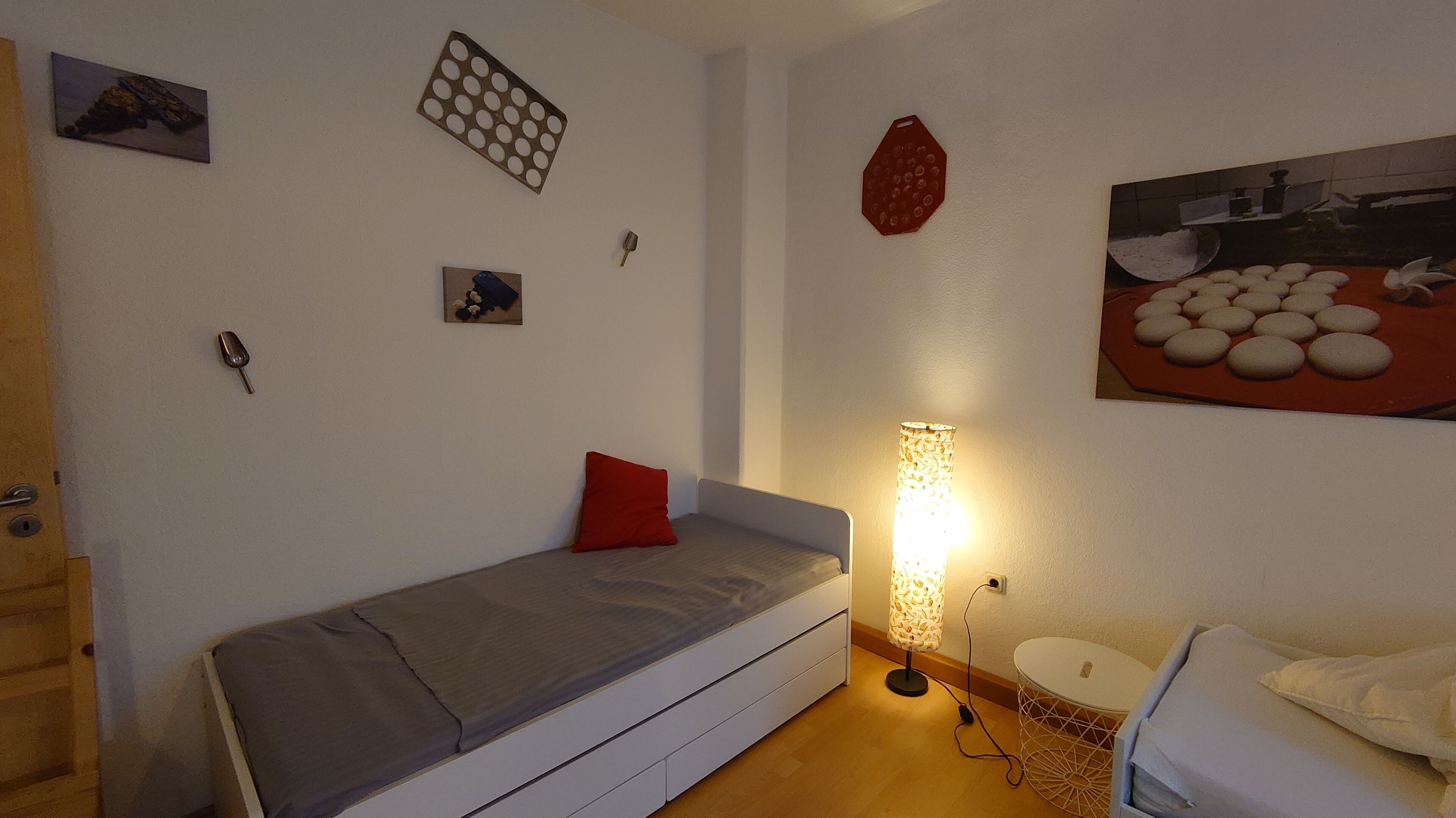 A small, compact room with a single bed, a bedside table, a lamp, and a wall-mounted shelf.