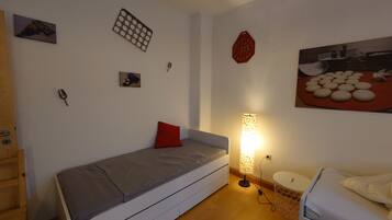 A small, compact room with a single bed, a bedside table, a lamp, and a wall-mounted shelf.