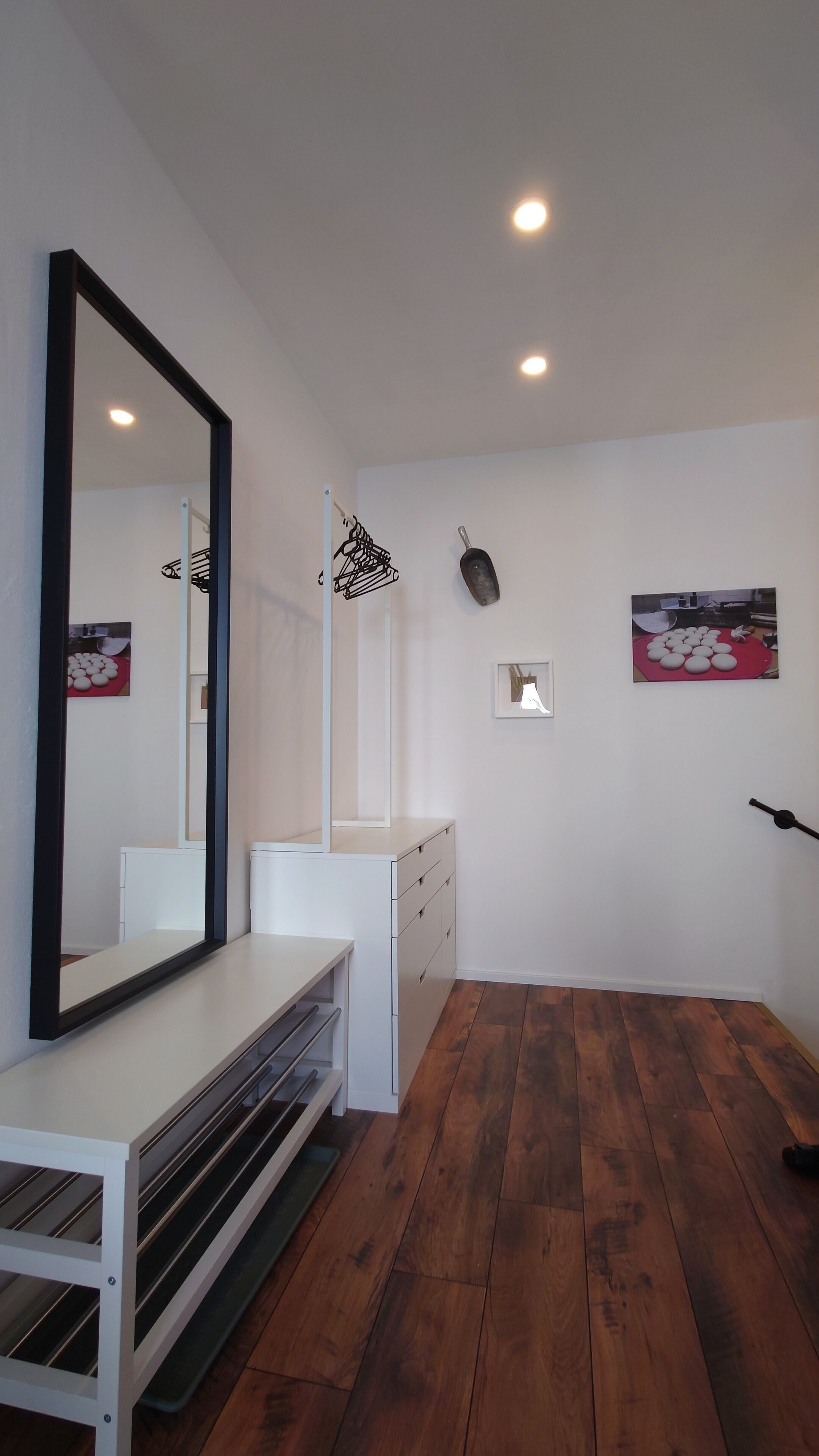 A modern bathroom with a large mirror, white cabinetry, wooden flooring, and a ceiling light.