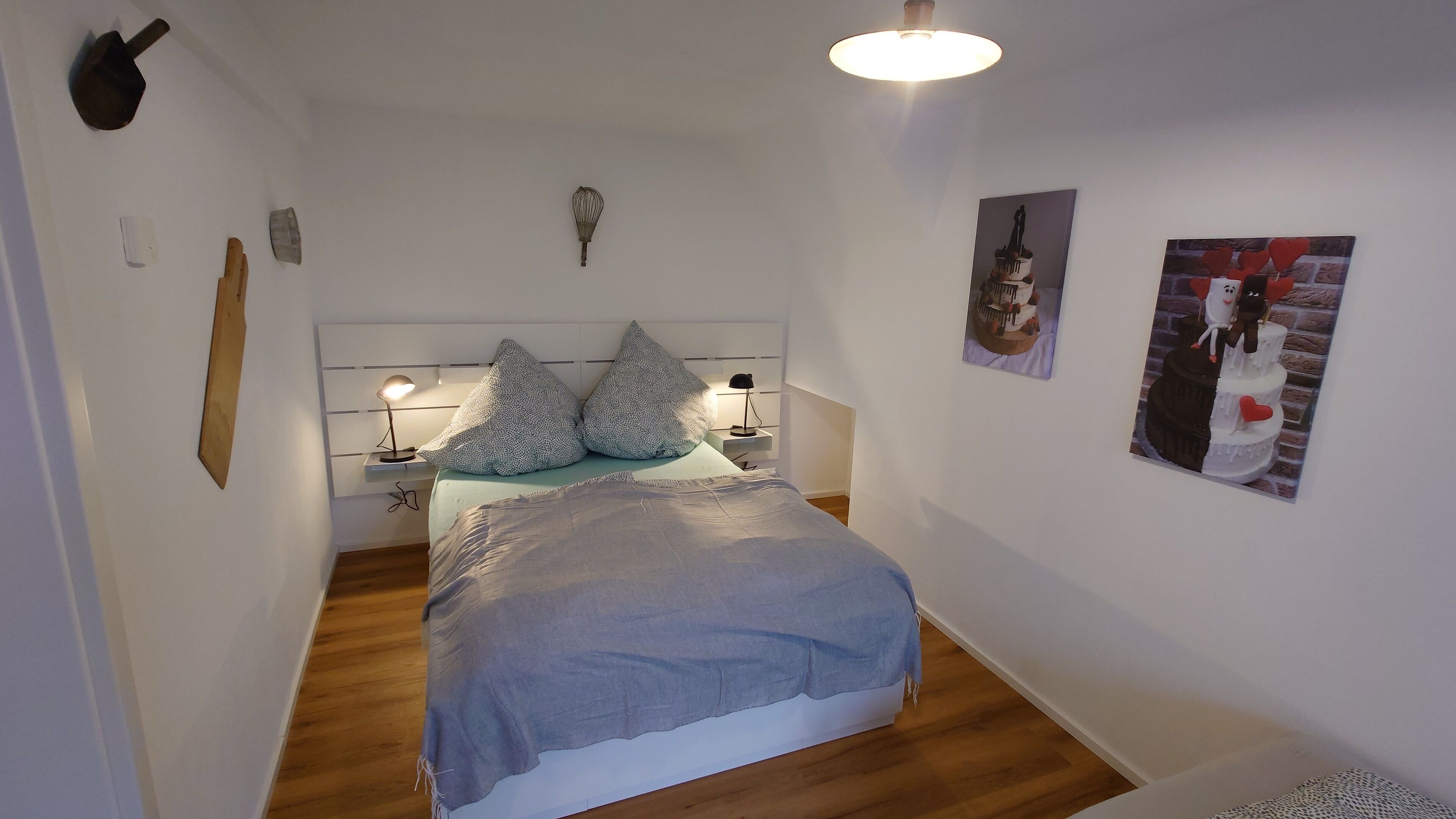 A bedroom with a bed, bedside lamps, a headboard, and wall decorations.