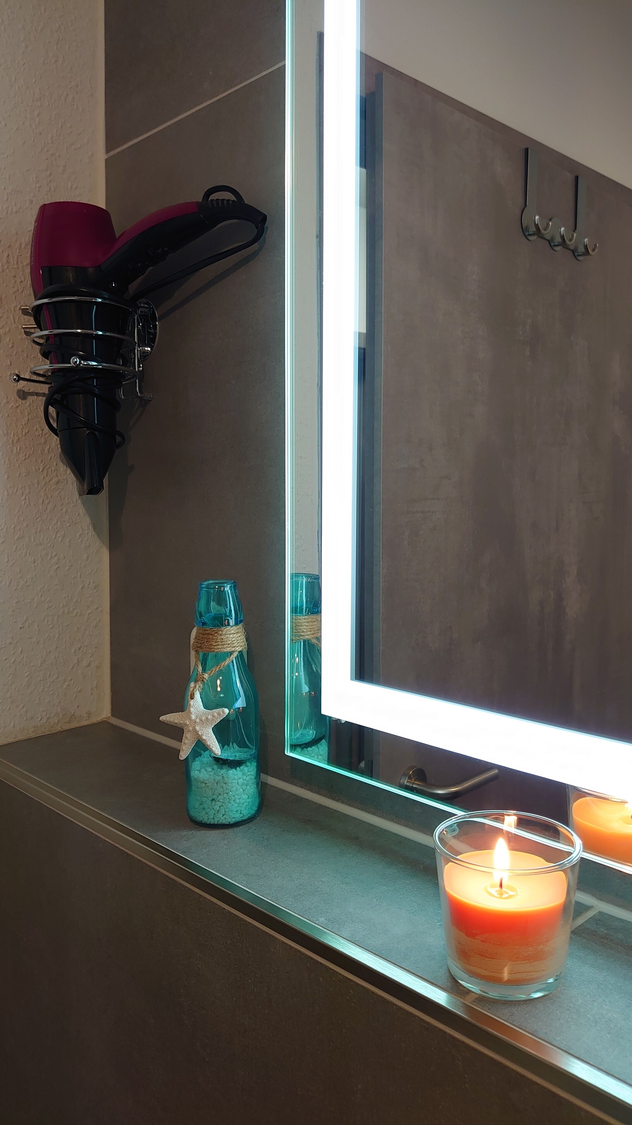 Un tocador de baño con espejo, un secador de pelo, una vela y botellas decorativas.