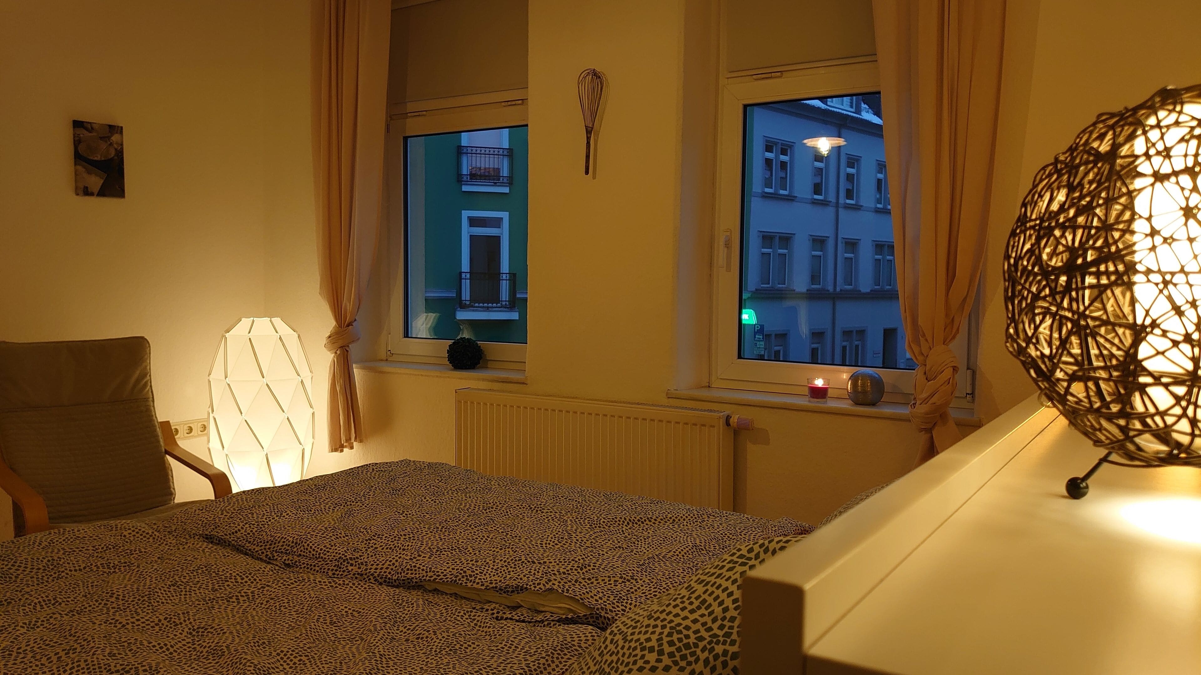 Ett sovrum med en säng, ett fönster med gardiner, ett element och en dekorativ lampa.