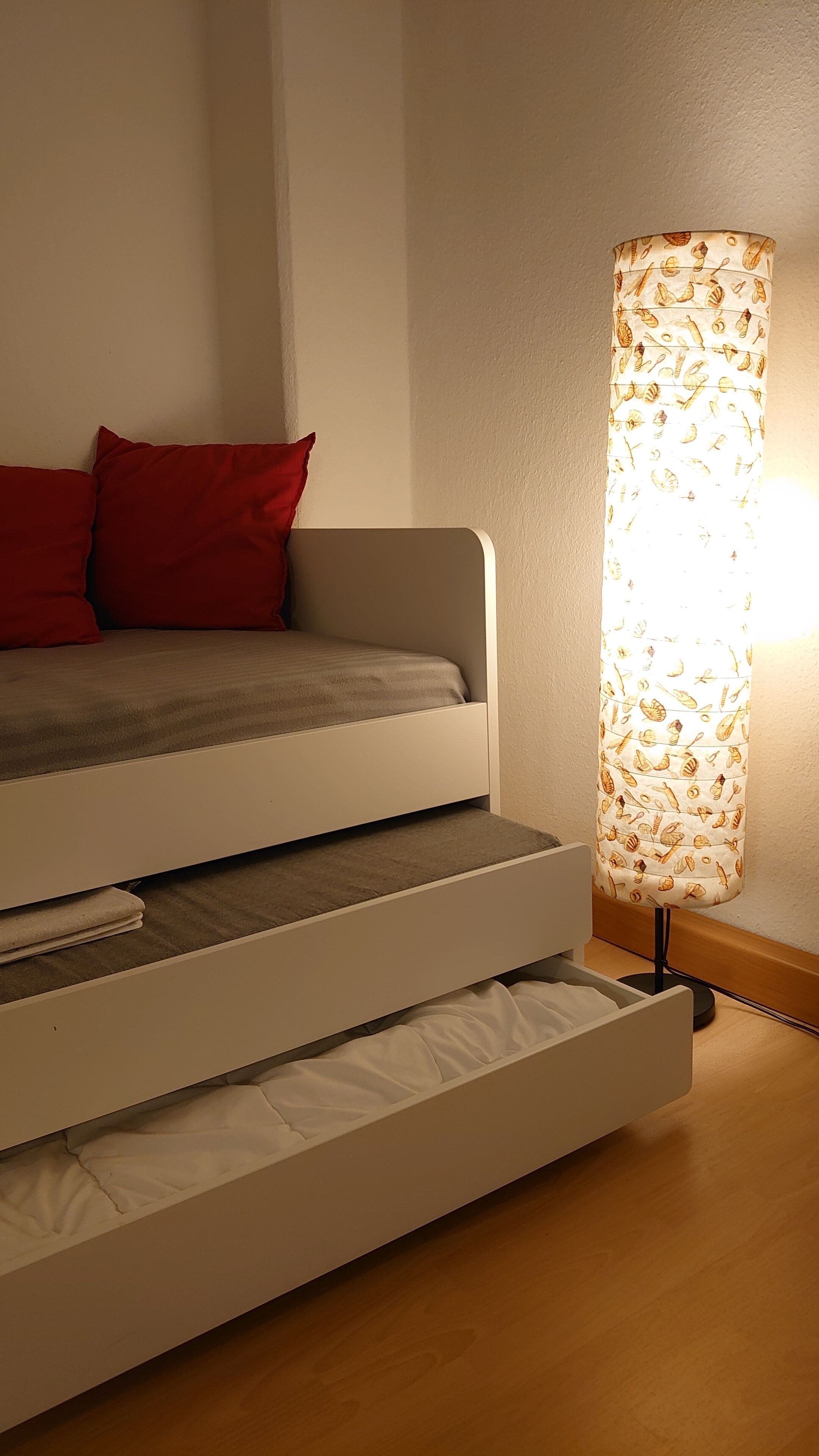 Ein Bett mit Stauraumschublade und einer Lampe mit Blättermotiv.