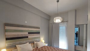 Et soveværelse med en stor seng, en sengegavl med vandrette træplanker, et natbord med en lampe og et spejl på væggen.