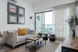 A modern living room with a sofa, coffee table, and artwork on the wall. - Tranquil Heights: Your Cozy Urban Getaway with Pool, Gym, and Spa (Santo Domingo)