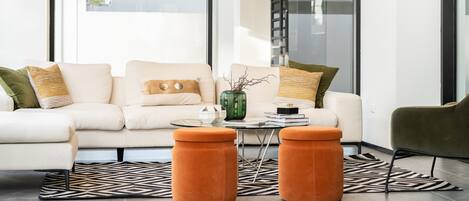 Ein modernes Wohnzimmer mit einer Couch, Poufs, einem Couchtisch und einem Bücherregal.