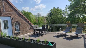 A deck with a brick wall, a table with chairs, and lounge chairs. - Haus im Seewind IV, 70 sqm - country house with large garden, near Friesenstrand (Butjadingen)