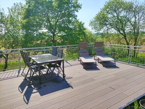 A deck with a table and chairs, surrounded by a metal railing, overlooking a green landscape.