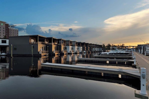 A marina with docked boats, a calm water surface, and a row of buildings with balconies.