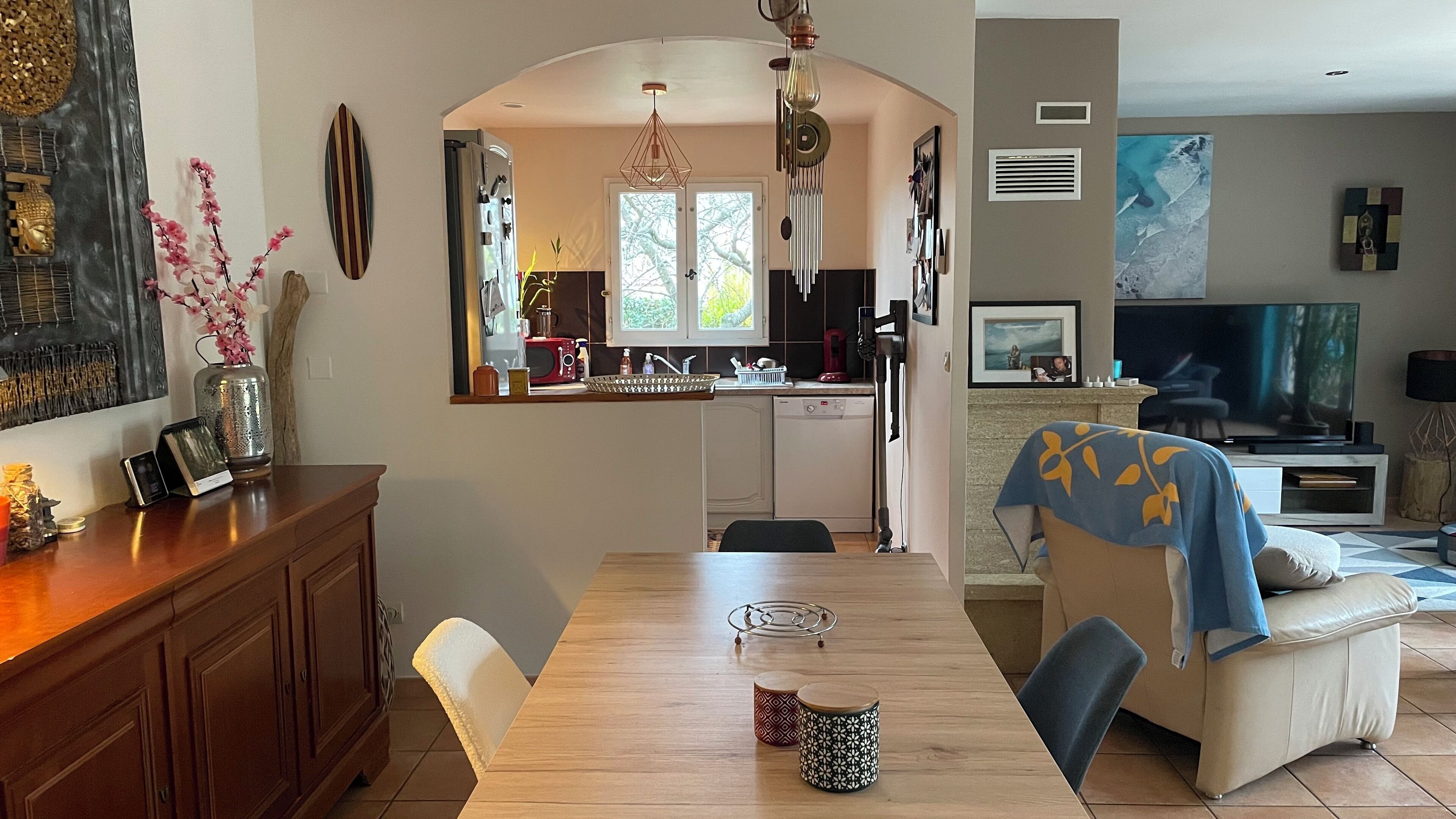 A modern kitchen with a central island, a dining area with a wooden table, and a living room with a sofa and TV.