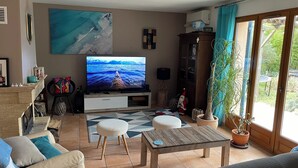 A living room with a large flat-screen TV, a sofa, a coffee table, and a potted plant. - Villa with pool, conveniently located between Arles Nimes and Avignion (Comps)