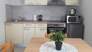 A compact kitchen with a sink, stove, microwave, and a small refrigerator. There is a dining table with chairs and a potted plant on the table. - Endless Horizont - Studio Apartment With Balcony (Razanac)
