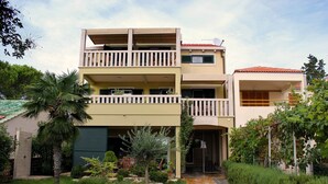 Ein zweigeschossiges Gebäude mit einem Balkon im oberen Geschoss, einer Garage und einem gepflasterten Weg zum Eingang.