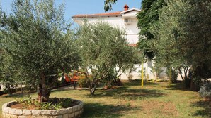 A garden with olive trees, a stone planter, and a white building with a red roof. - Ana Guest House - Double room with private terrace (Nin)