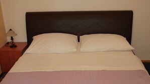 Una cama con cabecera oscura, dos almohadas y una colcha rosa.