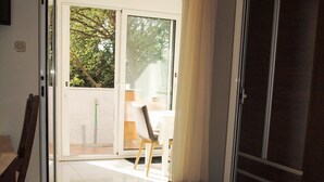 Un dormitorio con cama, armario, puerta corrediza de vidrio que da a un balcón y una pequeña mesa con silla.
