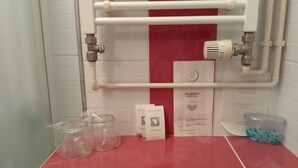 Un baño con pared de baldosas rojas, un perchero blanco y un gorro de ducha sobre el mostrador.