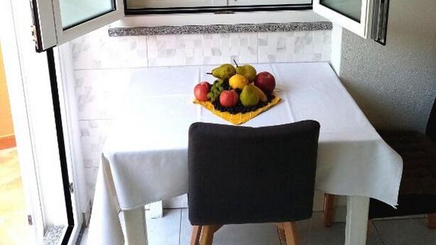 Un área de comedor con una mesa y sillas, un frutero sobre la mesa y una ventana con persianas.